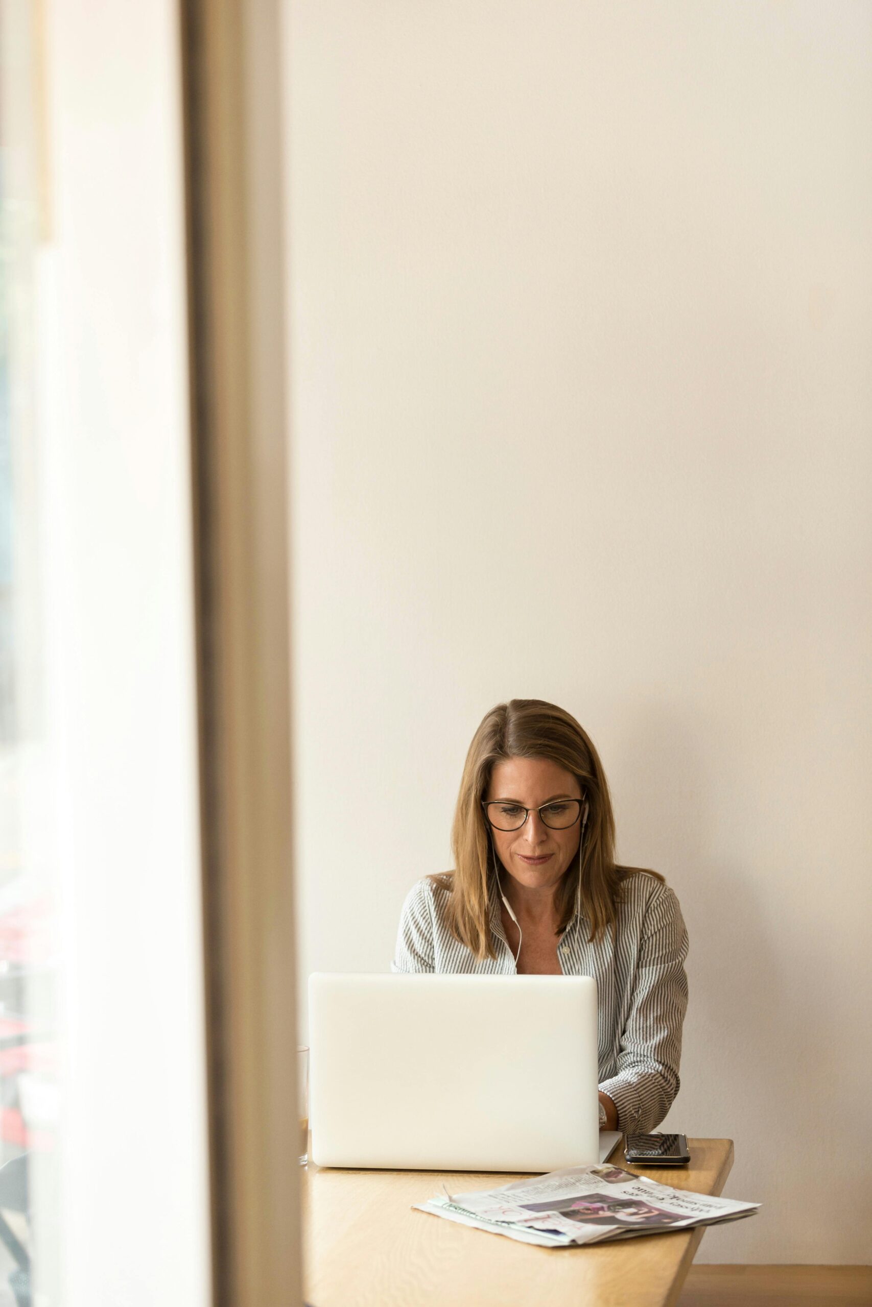 A woman with glasses is working on a laptop at a table. A valuable team member focused on strategy and content, driving success through digital expertise.
